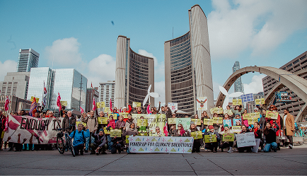 A large group of protesters hold signs and banners in front of Toronto City Hall, including one that reads Power up for climate solutions.